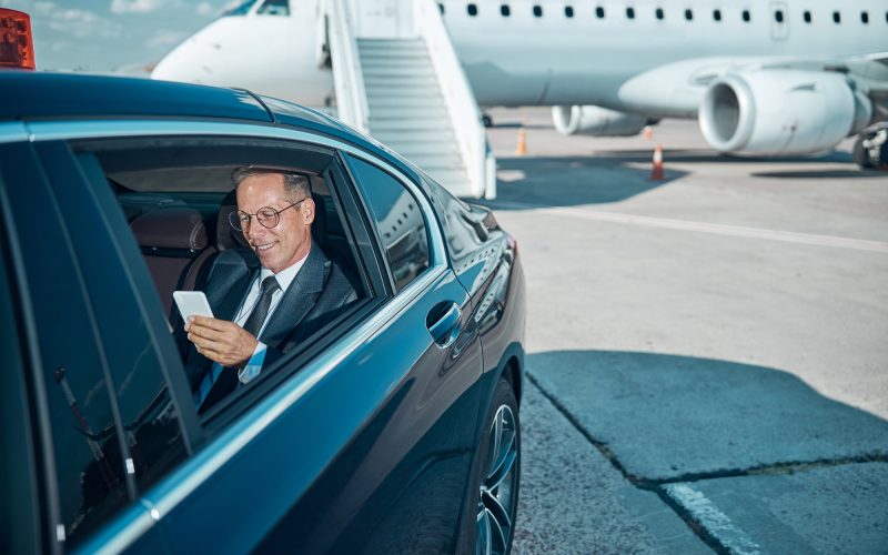 Smiling elegant man in glasses is using cell phone during transfer after trip by plane
